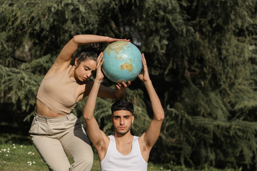 a-couple-in-a-pose-holding-a-globe-6963625 Man and woman artistically pose with a globe in a natural outdoor setting.