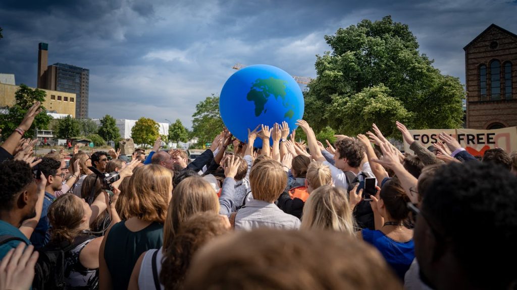 group-of-people-doing-a-demonstration-on-global-climate-and-environmental-issues-12111230 A diverse crowd participates in a climate protest in Berlin, Germany, raising a large Earth ball symbolizing environmental unity.